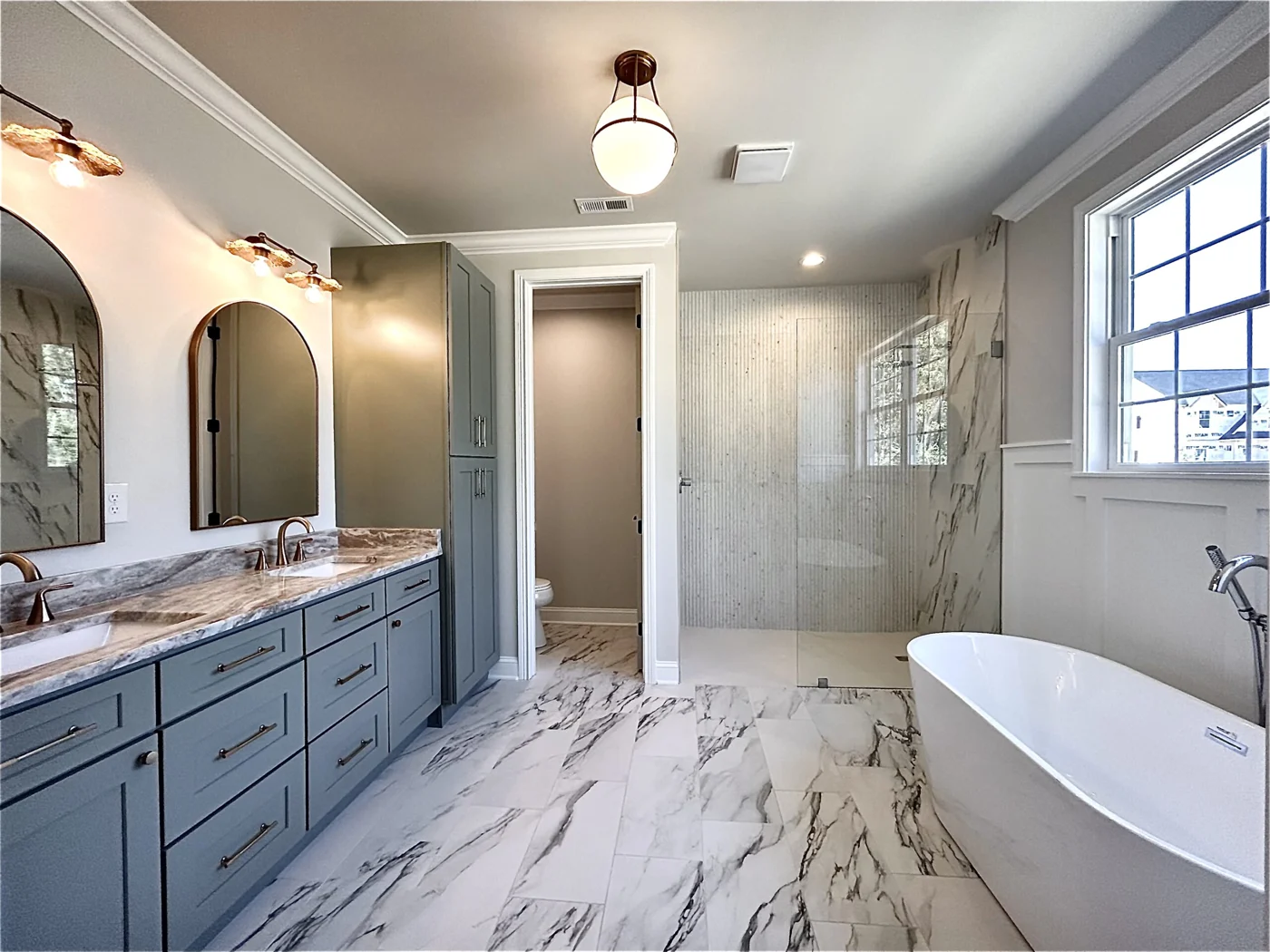 Portrait Homes bathroom with a freestanding tub, glass shower, and marble-pattern tile