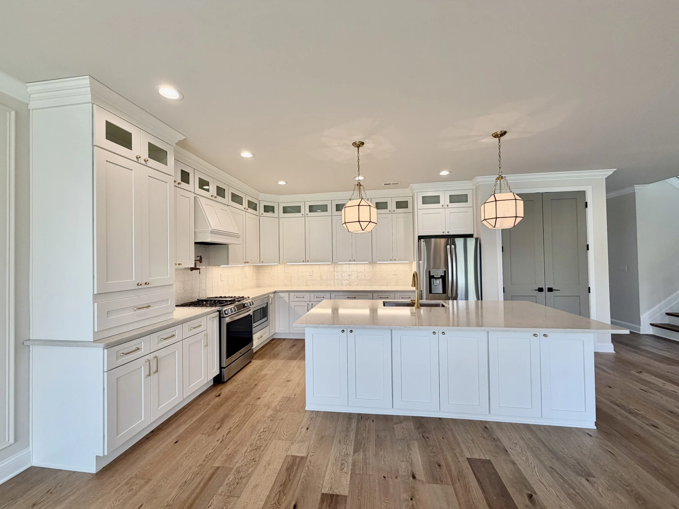 A Portrait Homes kitchen with white cabinetry, brass fixtures, pendant lighting, and a large island